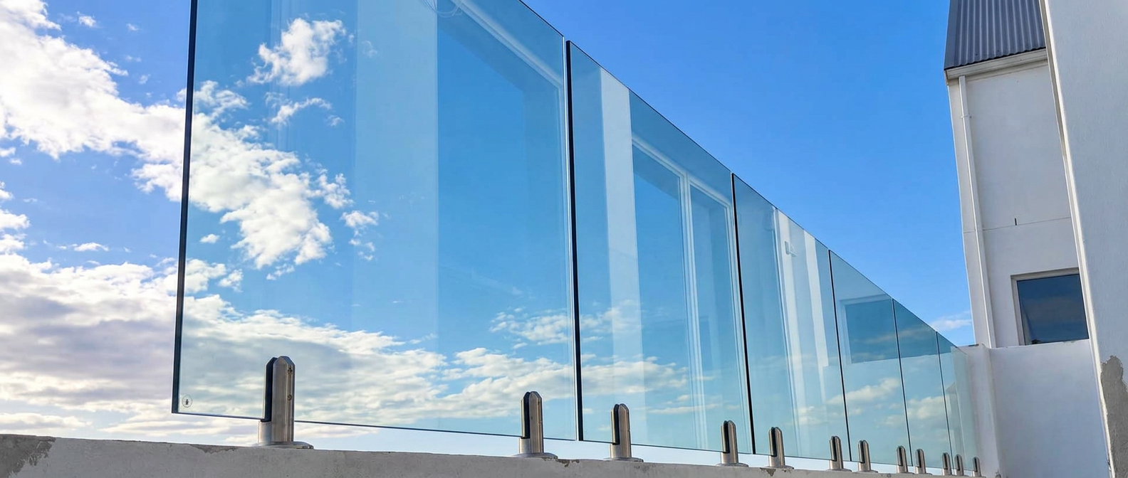 Frameless glass balustrade panels on the edge of a rooftop under a blue sky